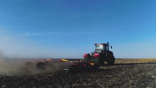 Letecký pohled na červený traktor s brázdovým systémem orající půdu na obdělávaném zemědělském poli, za ním sloup prašných cest, připravující půdu pro výsadbu nové plodiny — Stock video