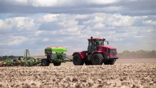 Luftaufnahme eines roten Traktors mit Eggenanlage, der Boden auf einem bewirtschafteten Feld pflügt, dahinter eine Säule von Staubspuren, die Erde für die Anpflanzung neuer Pflanzen vorbereitet — Stockvideo