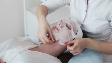 Güzellik uzmanı güzel bir bayanın yüzüne bez bir maske takar. Güzellik salonunun bayan müşterisi için yüz maskesi. Kozmetik ve kaplıca.