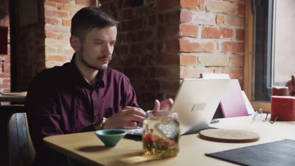 Portret van een aantrekkelijke jongeman aan het werk op zijn laptop in het café — Stockvideo