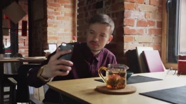 Genç adam Çin çay kafesinde cep telefonuyla selfie videosu kaydediyor.