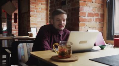 Kırmızı tişörtlü genç adam kafede Skype üzerinden konuşuyor.