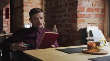 Genç adam kitap okuyor ve kafede Çin çayı içiyor.