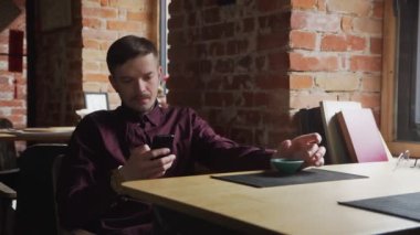 Genç yakışıklı adam çay içiyor ve kafede cep telefonunu kullanıyor.
