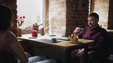 Kafede çay içerken gülümseyen ve konuşan genç bir çift.