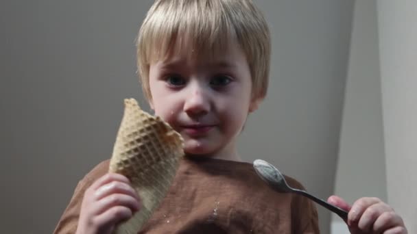 Widok na mały chłopiec siedzi na stole i je lody łyżeczką w kuchni w domu — Wideo stockowe