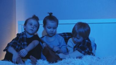 Üç küçük çocuk geceleri yatakta oturup gitar çalıyorlar.