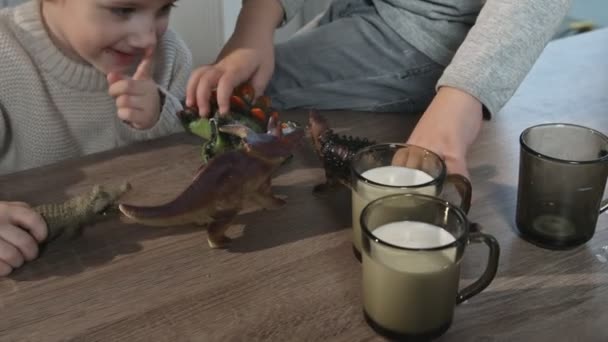 Two brothers play with toy dinosaurs on table at kitchen in home — Stock Video