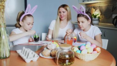 Bir anne ve kızları Paskalya yumurtası boyuyor. Mutlu aile Paskalya için hazırlanıyor. Paskalya günü tavşan kulağı takan sevimli küçük kızlar..
