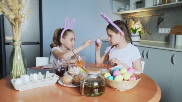 Paşte fericit. Două surori pictează ouă de Paşte. Copiii fericiti se pregatesc pentru Paste. Draguta fetiță copil care poartă urechi de iepuraș face ouă lupta pe camera — Videoclip de stoc