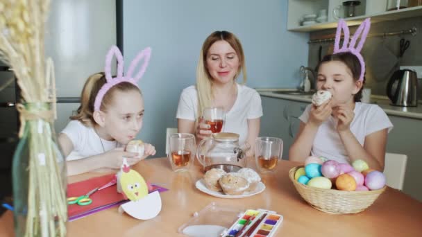 Feliz Páscoa. A preparar a família para a Páscoa. Mãe e suas filhinhas bebem chá e comem muffins — Vídeo de Stock