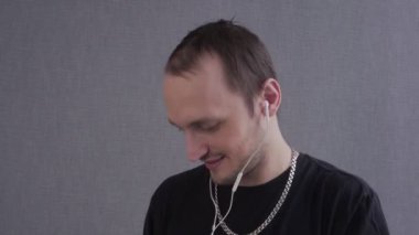 Altın zincirli genç adam telefonda kulaklıkla müzik dinliyor.