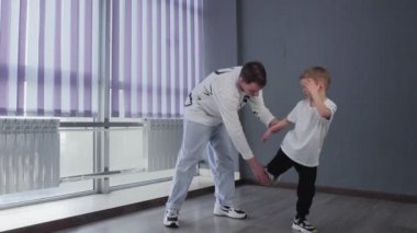Beyaz tişörtlü küçük çocuk öğretmeniyle break dans yapıyor.