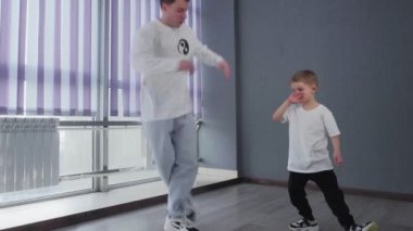 Beyaz tişörtlü küçük çocuk öğretmeniyle break dans yapıyor.