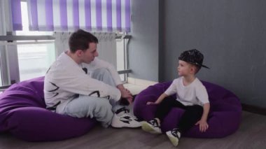 Beyaz tişörtlü ve siyah şapkalı çocuk dans dersinden sonra öğretmeniyle konuşuyor.