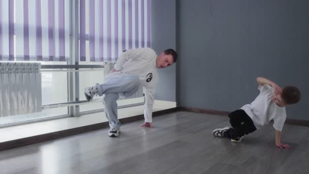 床の上で一緒に彼の先生と一緒に白いTシャツの男の子のダンスのブレークダンス — ストック動画