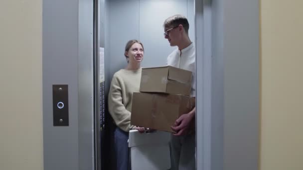 若いカップルがエレベーターから出て段ボール箱と折りたたみ椅子で新しいアパートに移動します — ストック動画
