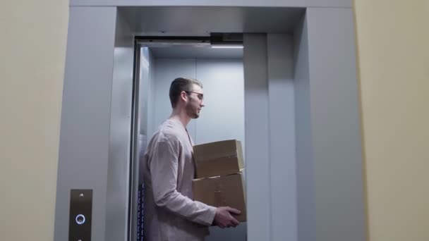 Молодая пара выходит из лифта с картонными коробками, переезжает в новую квартиру — стоковое видео