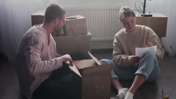 Glückliches Paar packt Kartons, bereitet sich auf den Umzug vor, Familie sitzt am Umzugstag auf dem Fußboden im Wohnzimmer — Stockvideo