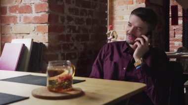 Genç işadamı kafede oturuyor ve çay molası verirken telefonla konuşuyor.