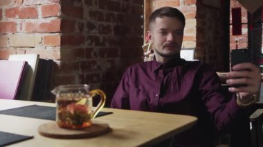 Genç adam Çin çay kafesinde cep telefonuyla selfie çekiyor.