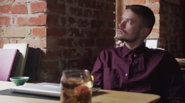 Çekici genç iş adamı kafeteryada oturup bilgisayarını kapatmış düşünüyor.