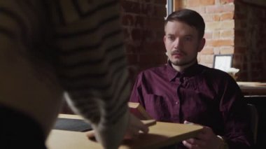 Garson, kafede kitap okuyan adama çay getiriyor.