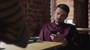 Genç yakışıklı adam çay içiyor ve kafede cep telefonunu kullanıyor.