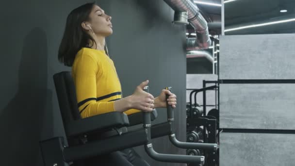 Beatiful Fitness Vrouw in gele top Oefening op Gym. Vrouw met koptelefoon doet opknoping Leg Oefening — Stockvideo
