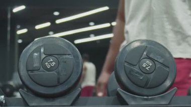 Afrikalı adam spor salonunda bir dambılı alır ve kaldırır.