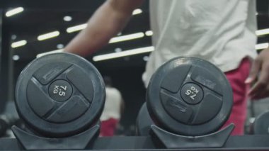 Afrikalı adam spor salonunda iki dambılı alır ve kaldırır.