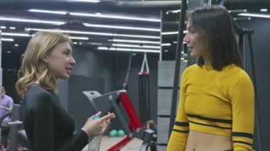Spor salonunda iki genç kadın konuşuyor. Sarışın ve esmer kadınlar hoşça kal der ve giderler.