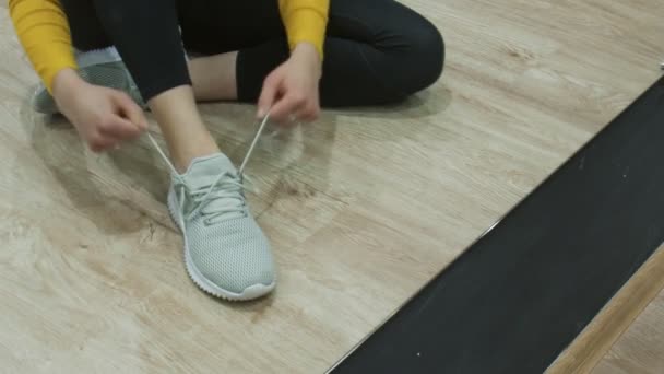 Close-up van vrouw zit op de vloer en bindt haar snikers — Stockvideo