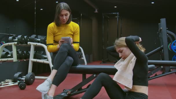 Pelatih pribadi perempuan berbicara dengan seorang klien wanita di gym dan menunjukkan catatan latihan berikutnya — Stok Video