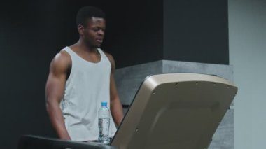 İdman yapmadan önce ısınmak için koşu bandında yürüyen kaslı Afro-Amerikalı bir adam.