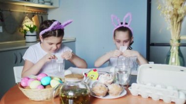 Paskalya günü tavşan kulağı takan komik kız kardeşler yumurta boyuyor.