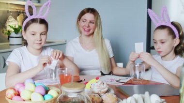 Bir anne ve kızları Paskalya yumurtası boyuyor. Mutlu aile Paskalya için hazırlanıyor. Paskalya günü tavşan kulağı takan sevimli küçük kızlar..