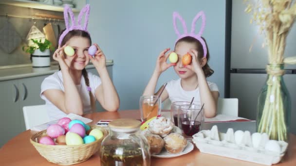 Щасливого Великодня. Дві сестри малюють великодні яйця. Щасливі сімейні діти готуються до Великодня. Симпатична маленька дівчинка в вухах кролика позує з кольоровими яйцями на камеру — стокове відео
