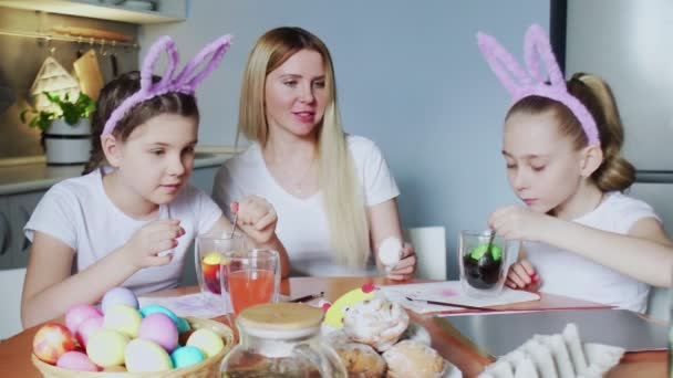 Una madre y sus hijas pintando huevos de Pascua. Familia feliz preparándose para la Pascua. Lindas niñas usando orejas de conejo en el día de Pascua. — Vídeo de stock