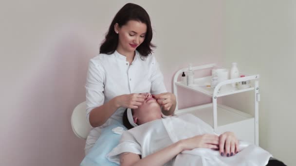Cosmetóloga mujer elimina almohadillas de colágeno de los ojos del cliente mujer en salón de belleza clínica. — Vídeos de Stock