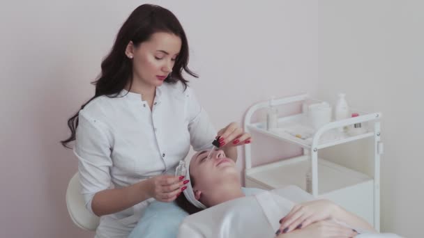 Cosmetologist εφαρμόζει peeling λοσιόν στο πρόσωπο πελάτη γυναίκα στο σαλόνι ομορφιάς κλινική. Πορτρέτο της γυναίκας παίρνει ιατρική καθαρισμό προσώπου κοσμετολογία δέρμα ακμής διαδικασία σε spa. — Αρχείο Βίντεο