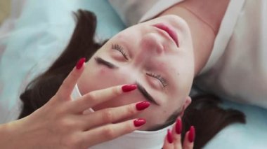 Kanepede gözleri kapalı yatan bir kadının yüzüne krem süren güzellik uzmanının en iyi görüntüsü..