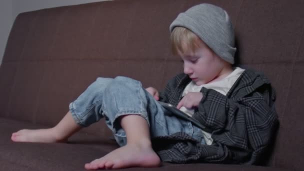 Barn pojke leker med surfplatta hemma. Kid Använda tablett sittande på en soffa — Stockvideo