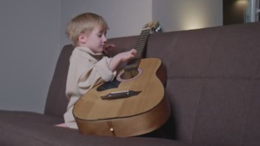 Küçük çocuk odasında gitar çalıyor.
