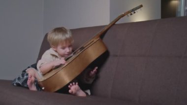 Küçük çocuk gitar çalar ve şarkı söyler..