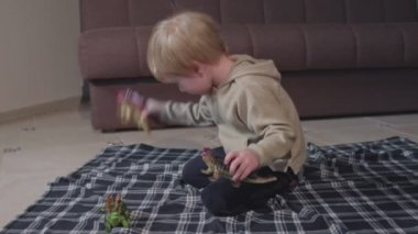 Sarışın çocuk, evde dinozorlarla oynuyor.