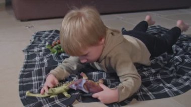 Küçük çocuk yerde oyuncak dinozorlarla oynuyor.