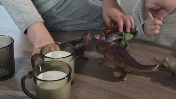 Два брата играют с игрушечными динозаврами на столе на кухне в доме — стоковое видео