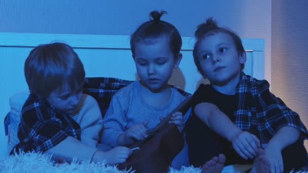 Trois petits garçons s'assoient sur le lit et jouent de la guitare dans la chambre la nuit — Video