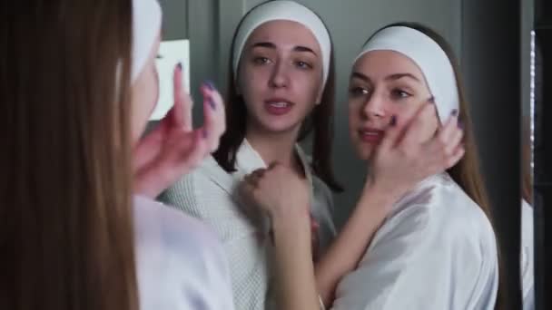 Две девушки смотрят в зеркало после косметической косметологии — стоковое видео